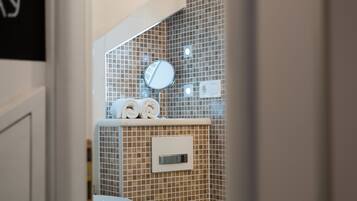 Un baño con pared de azulejos, un espejo y dos toallas enrolladas en un estante.