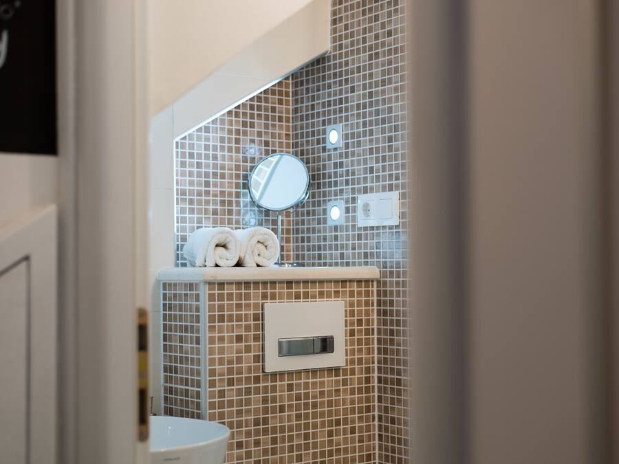Un baño con pared de azulejos, un espejo y dos toallas enrolladas en un estante.