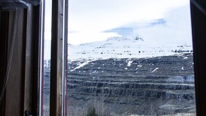 A window view of a mountainous landscape with snow-covered peaks and a forested valley. - Fossardalur Guesthouse - Hostel (Djupivogur)