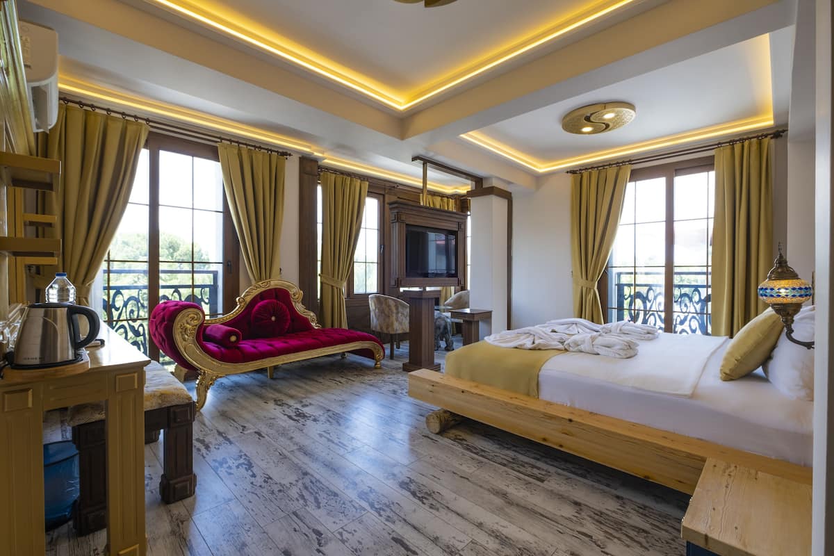 A hotel room with a wooden bed, a red velvet chair, a television, and a balcony with curtains.