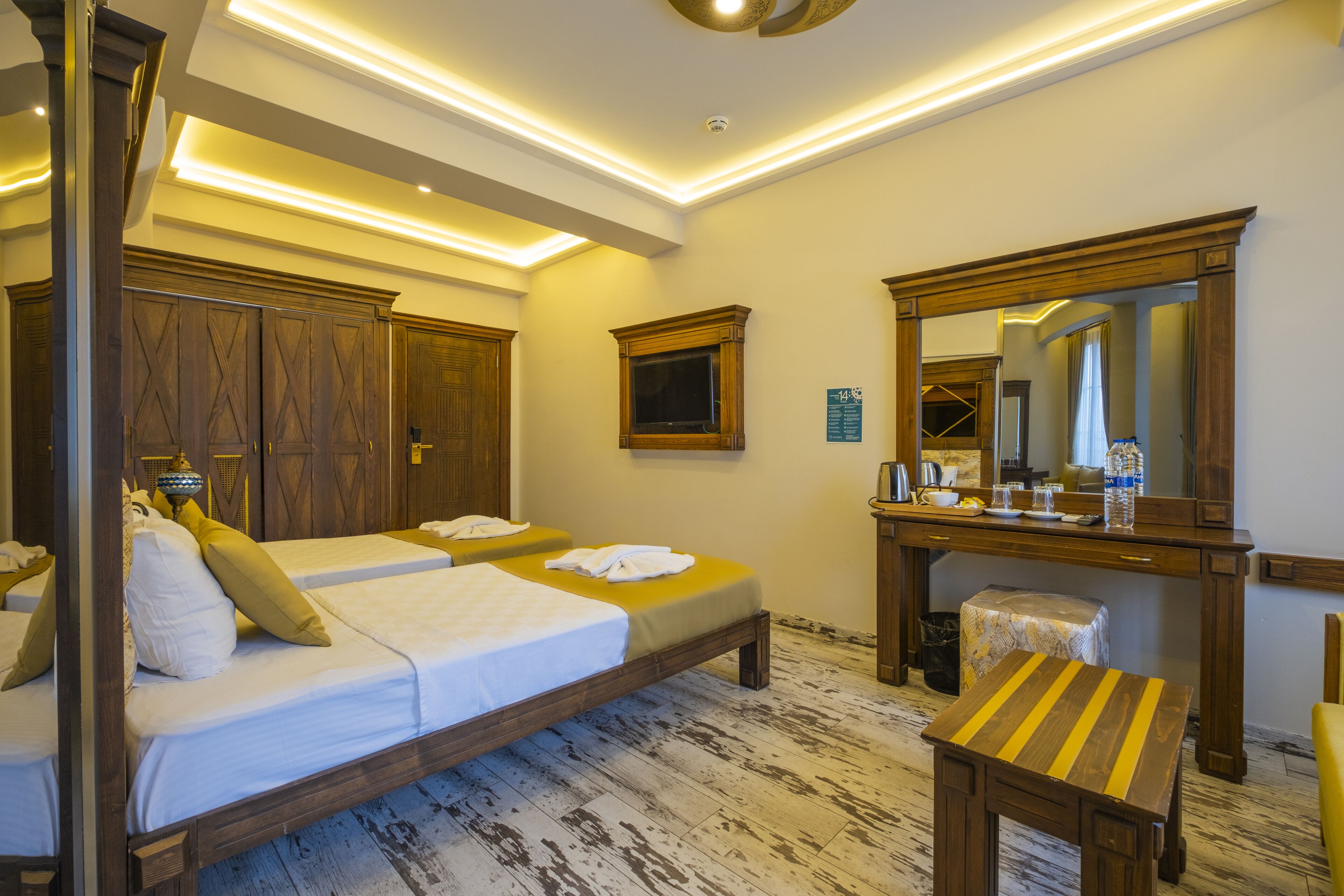 Una habitación de hotel con dos camas, un escritorio de madera, un espejo y un taburete pequeño.