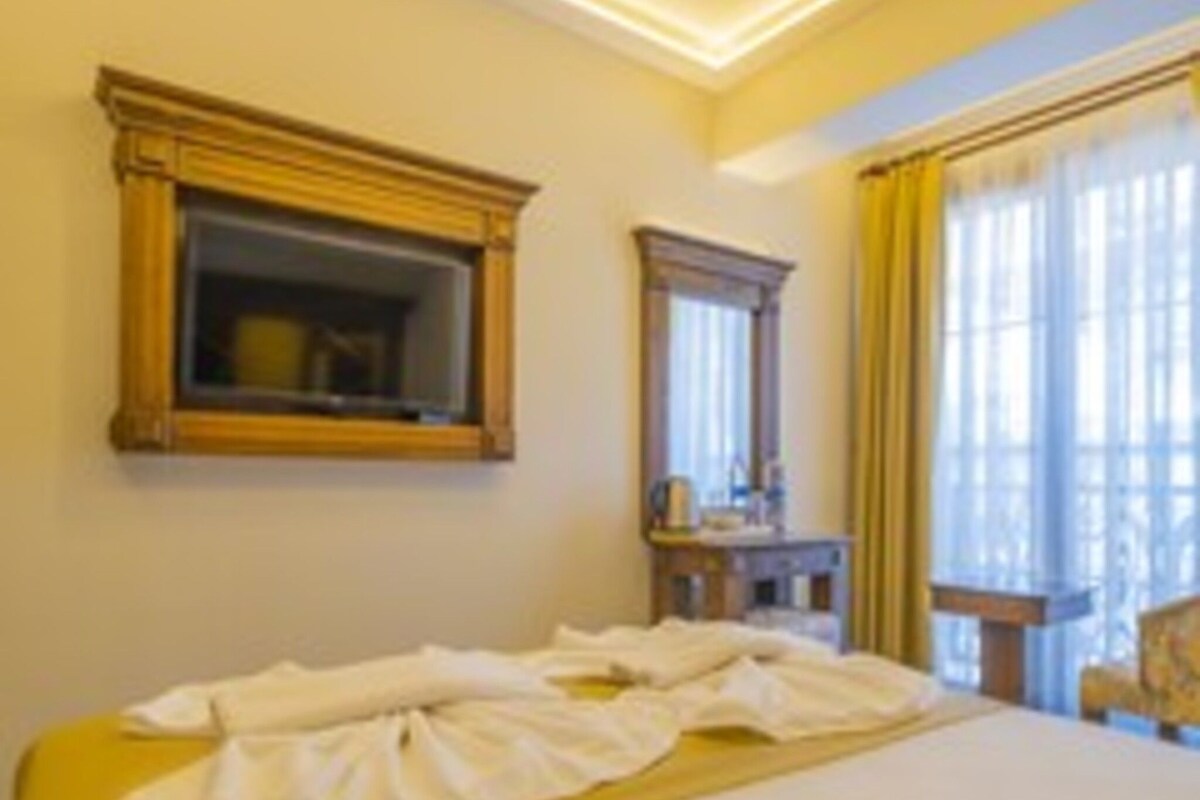 Une chambre d’hôtel avec un lit, une table de chevet, un miroir et une fenêtre avec des rideaux.