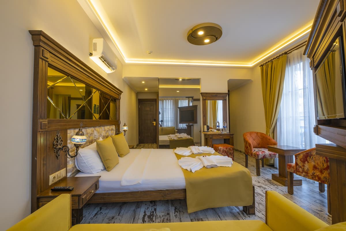 A hotel room with a large bed, a sitting area with a chair and table, a television, and a mirror.