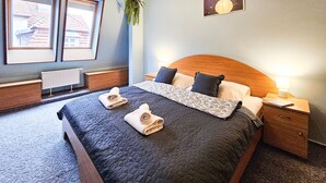 Een netjes opgemaakt bed met een gewatteerde spreidek, twee nachtkastjes, een nachtkastje met een lamp, een ingelijste foto aan de muur en een hangende plant.