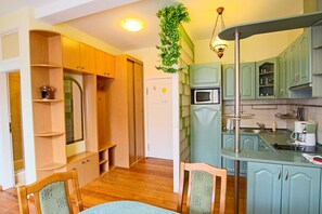 Een kleine keuken met houten kastjes, een magnetron en een hangende plant.