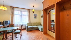 Een kamer met een eettafel, stoelen, een bank, een televisie en een spiegel.