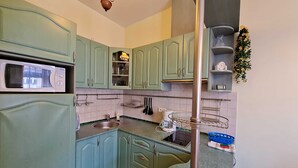 Een keuken met groene kastjes, een magnetron, een spoelbak en een hangende plant.