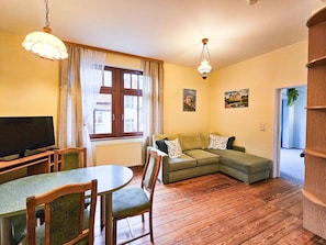Een woonkamer met een televisie, een eettafel met stoelen, een bank en een hanglamp.