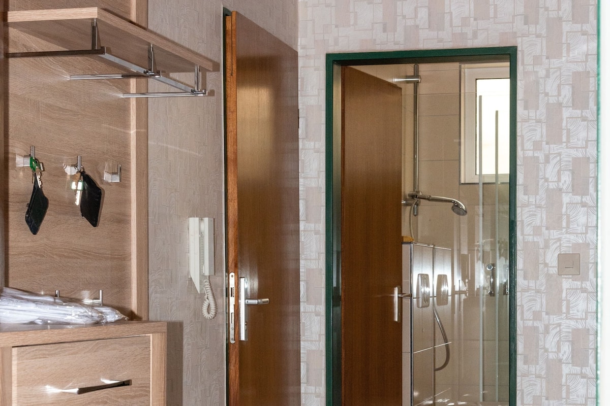 A modern bathroom with a wooden vanity, a glass shower enclosure, and a green-framed door leading to a shower area.