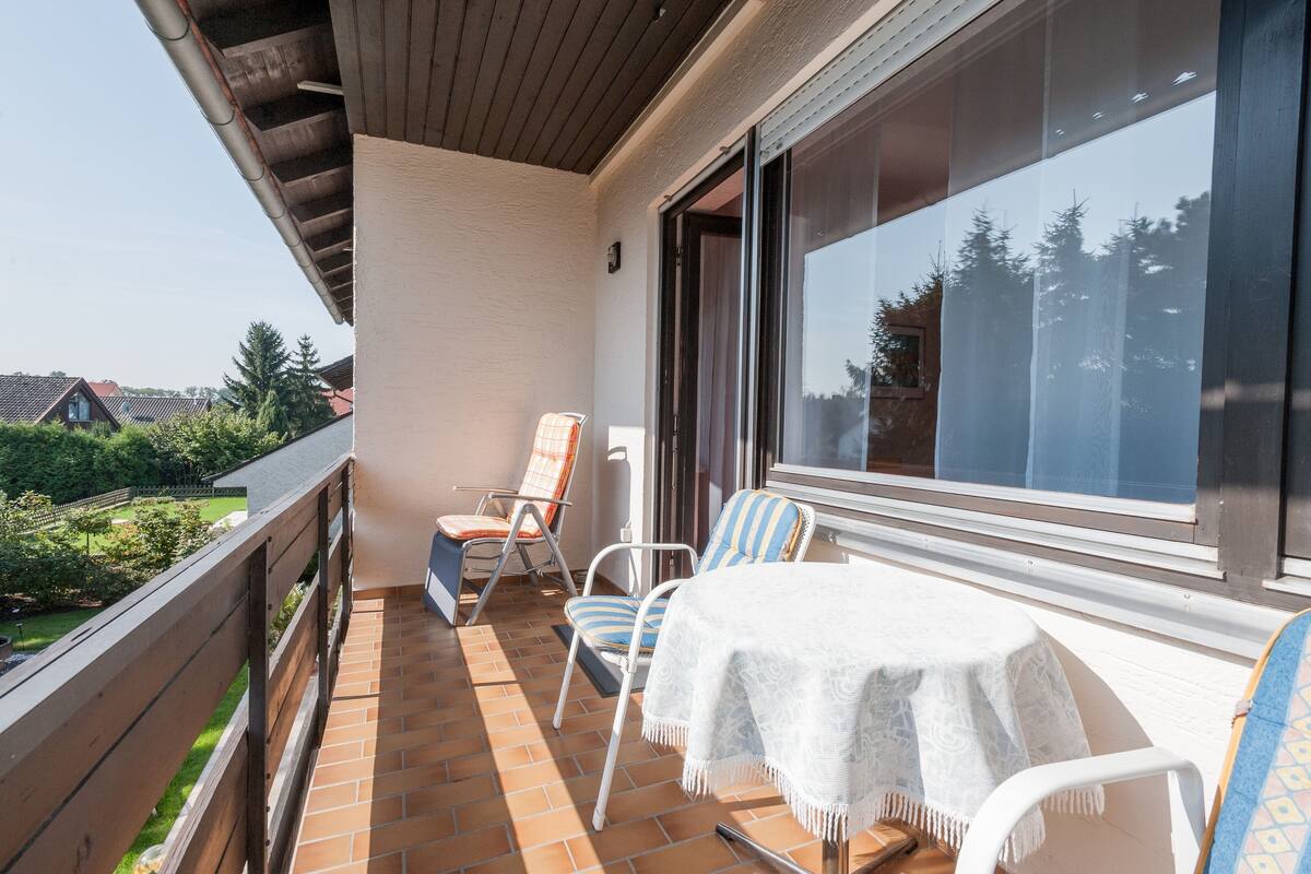 A balcony with a table and chairs, a view of the garden, and a large window.
