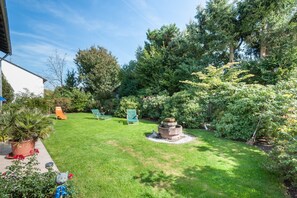 Un jardín bien cuidado con un hogar para fuego, sillas verdes y una variedad de plantas.