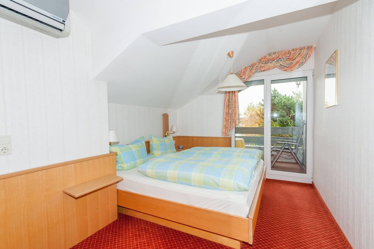 A bedroom with a wooden bed, a nightstand, a lamp, and a view of the outdoors through a sliding glass door.