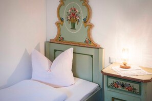 Een bed met witte beddengoed, een nachtkastje met een lamp, en een decoratief kunstwerk erboven.