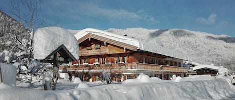 A wooden chalet with a balcony, surrounded by snow-covered hills.