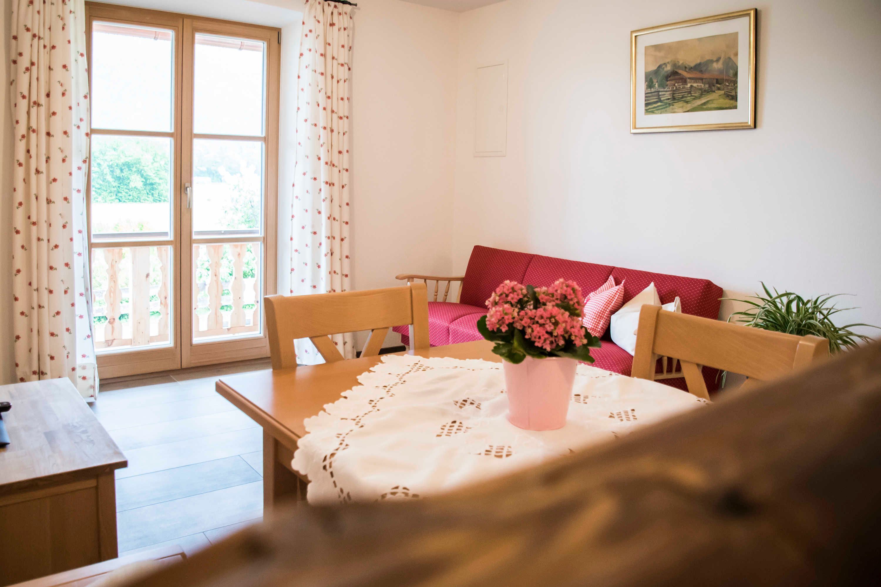 A room with a wooden table, a red sofa, a potted plant, and a painting on the wall.