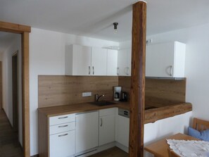 Cocina compacta con armarios blancos, encimera de madera, cafetera y lavabo.