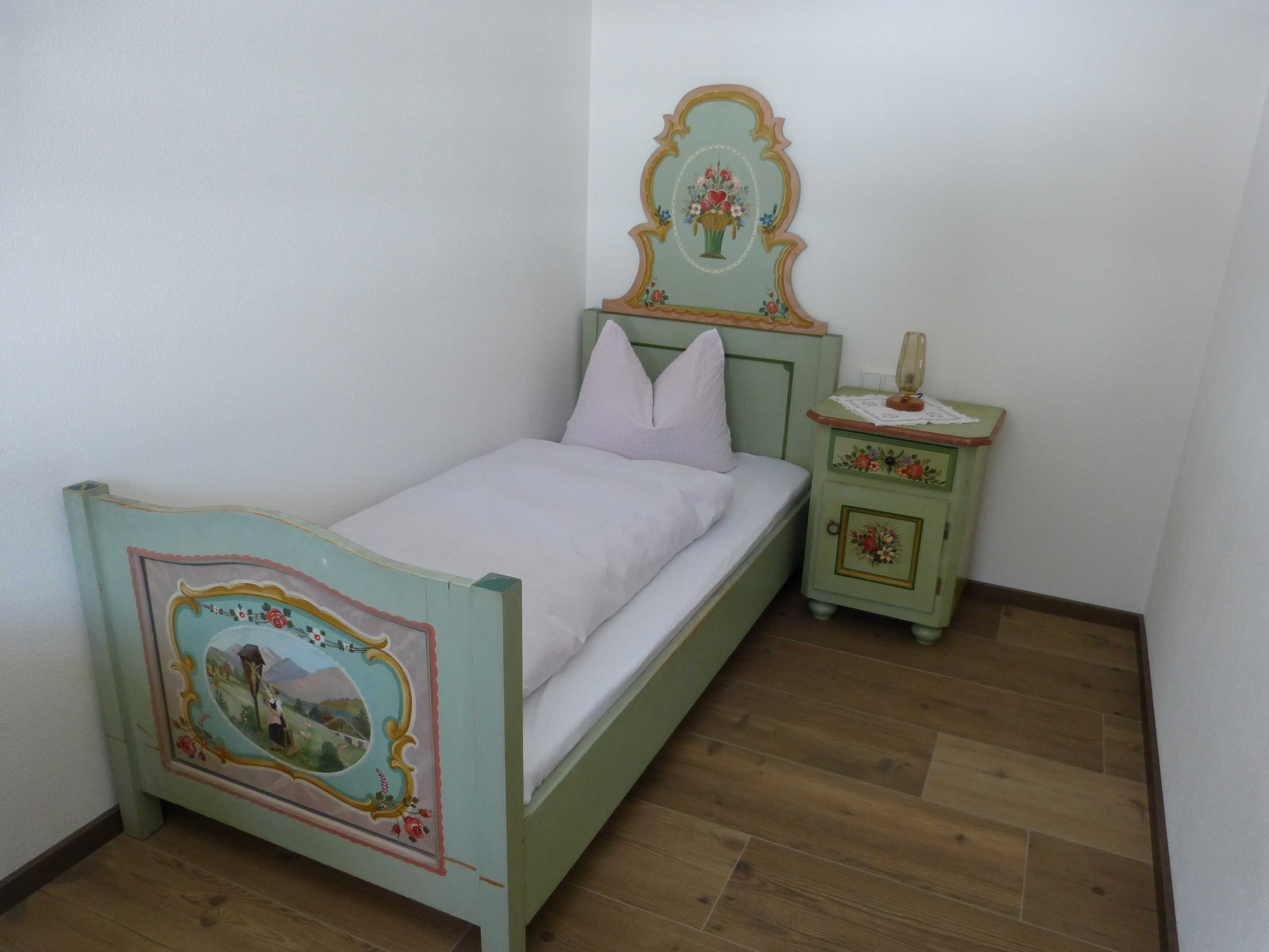 Una cama individual con cabecera, una mesita de noche con lámpara y un mueble auxiliar con un adorno.