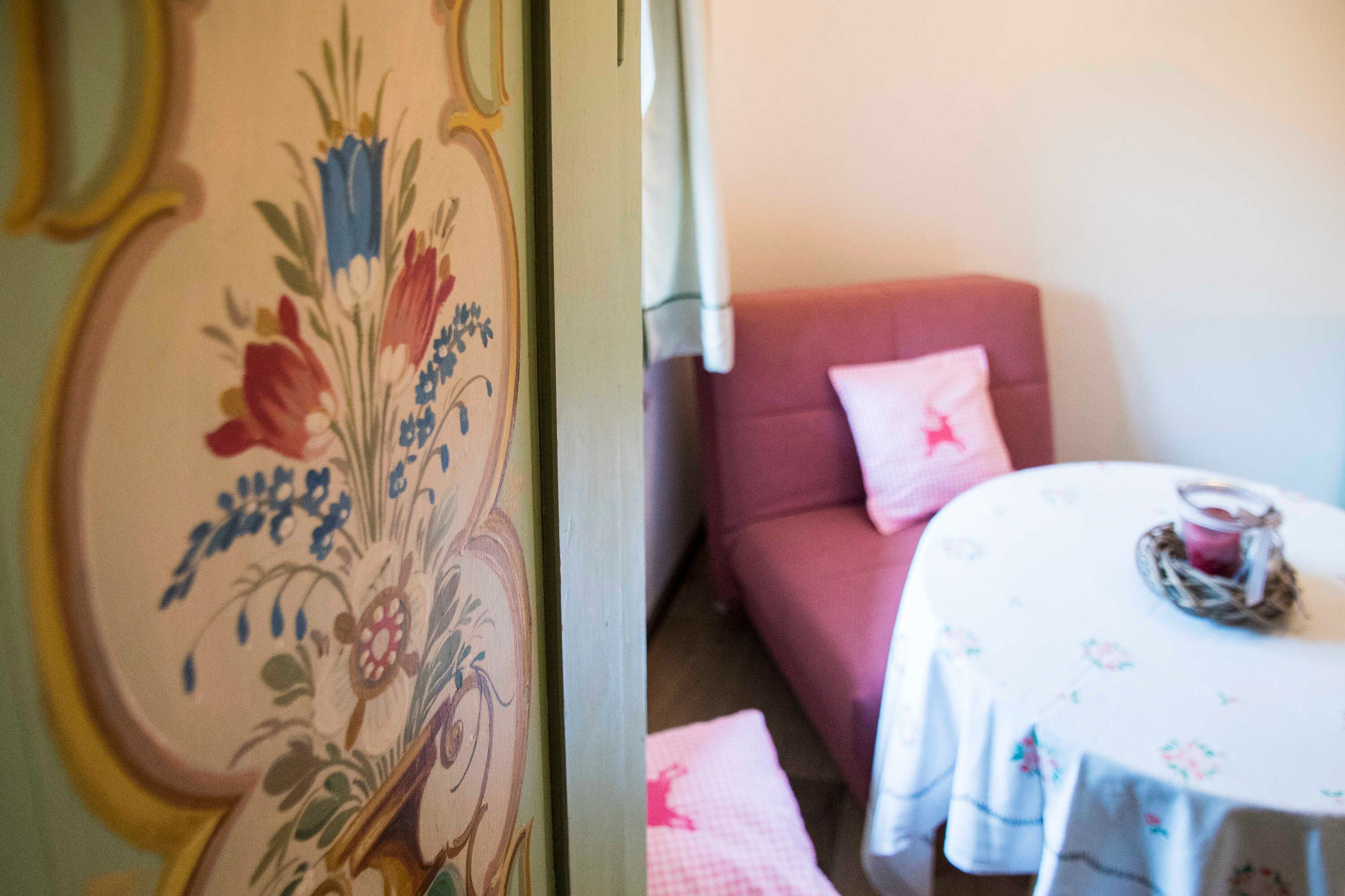 Ein Zimmer mit einer türverziert mit floralem Muster, einem rosafarbenen Sofa mit Kissen und einem runden Tisch mit Kerze.