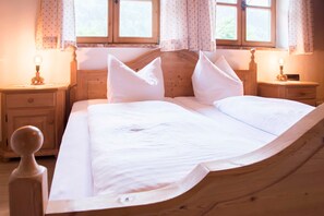 Una cama de madera con ropa de cama blanca, dos mesitas de noche con lámparas y una ventana con cortinas.