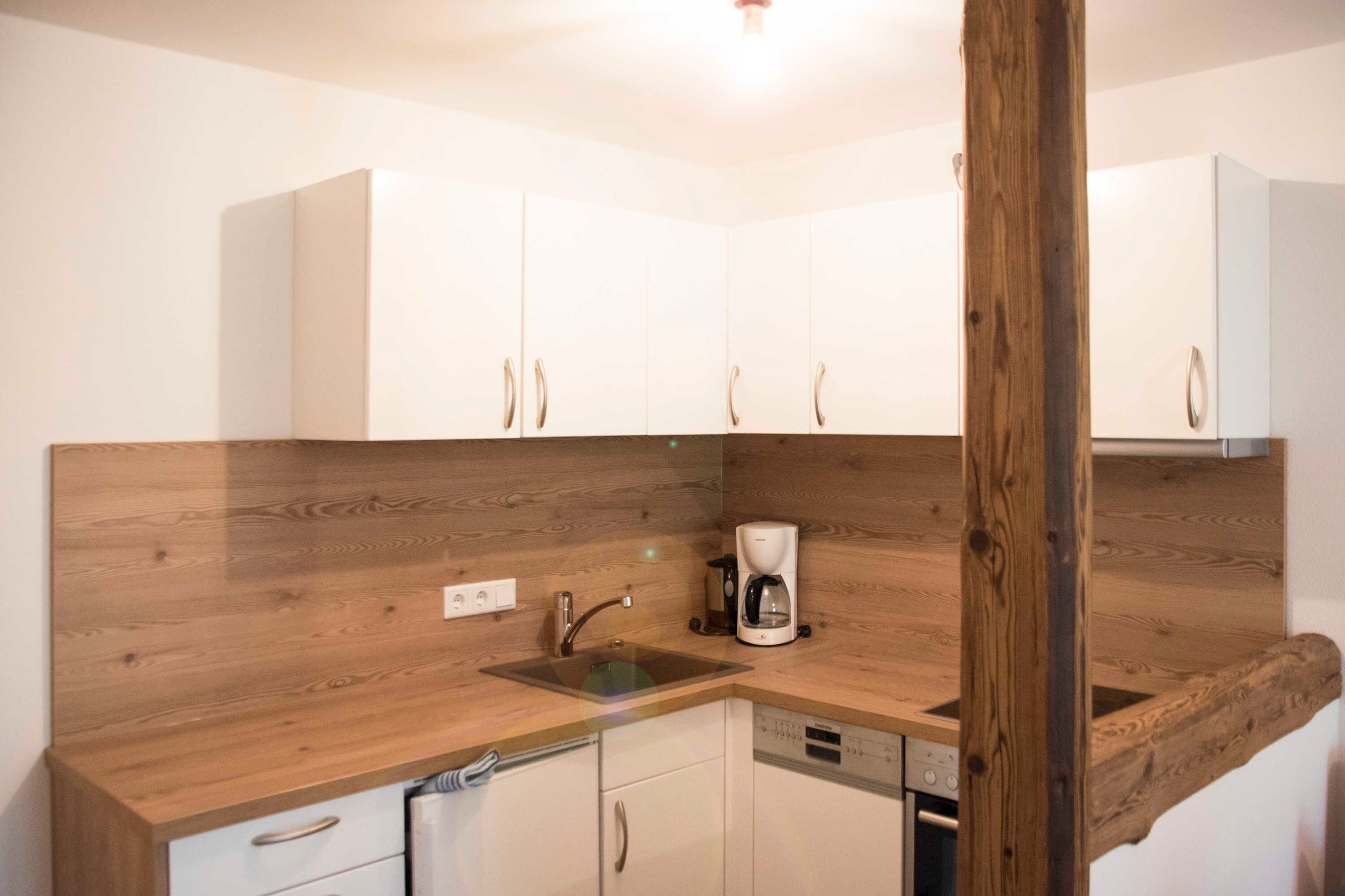 Une cuisine avec des plans de travail en bois, des meubles blancs, une machine à café et un lave-vaisselle.