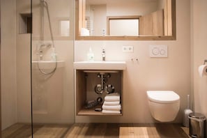 Een badkamer met een douchecabine van glas, een wastafel met spiegel erboven, een toilet en een prullenbak.
