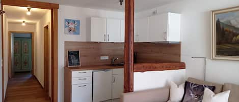 Een knus woongedeelte met een kitchenette, een eethoek en een bank met decoratieve kussens.