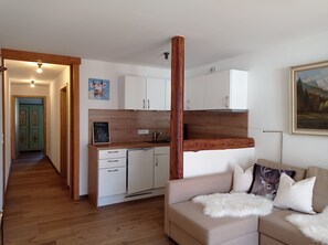 Een knus woongedeelte met een kitchenette, een eethoek en een bank met decoratieve kussens.