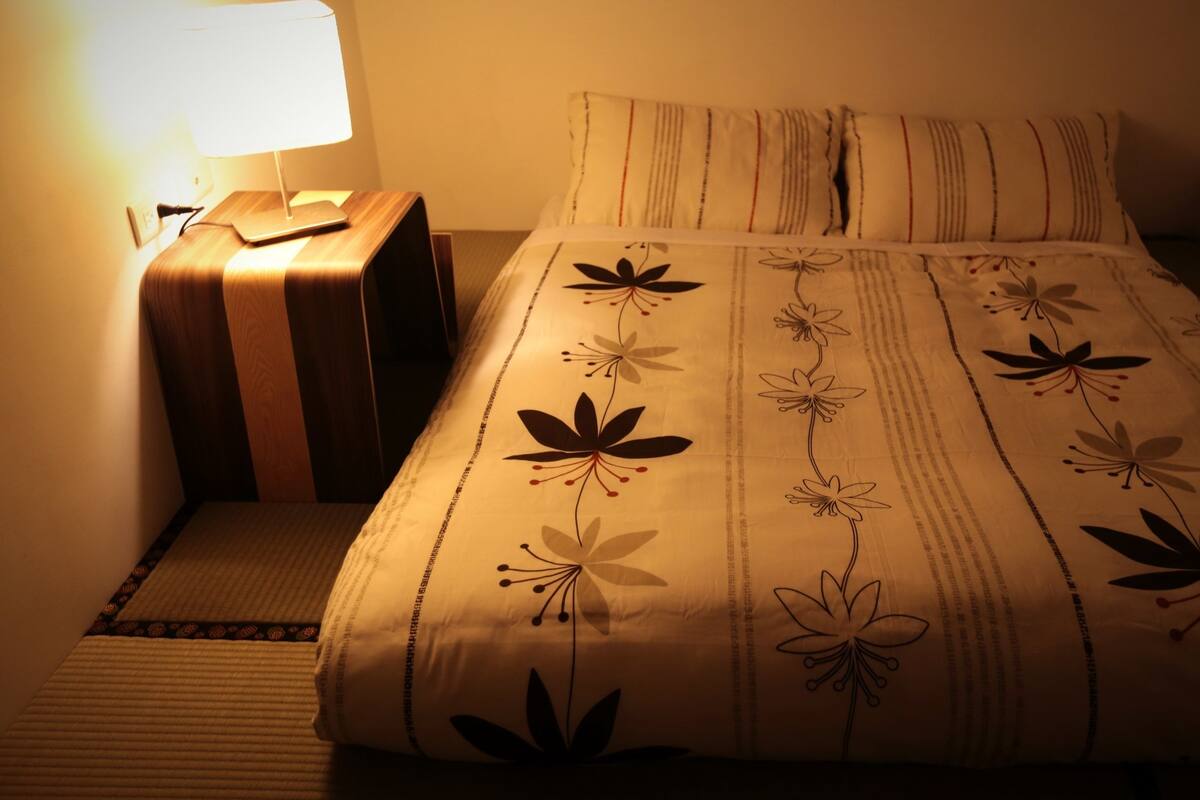 A neatly made bed with floral bedding, a bedside lamp, and a wooden nightstand.