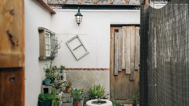 A narrow courtyard with potted plants, a wooden door, and a tiled wall. - Kinba Guest House (Jinning)