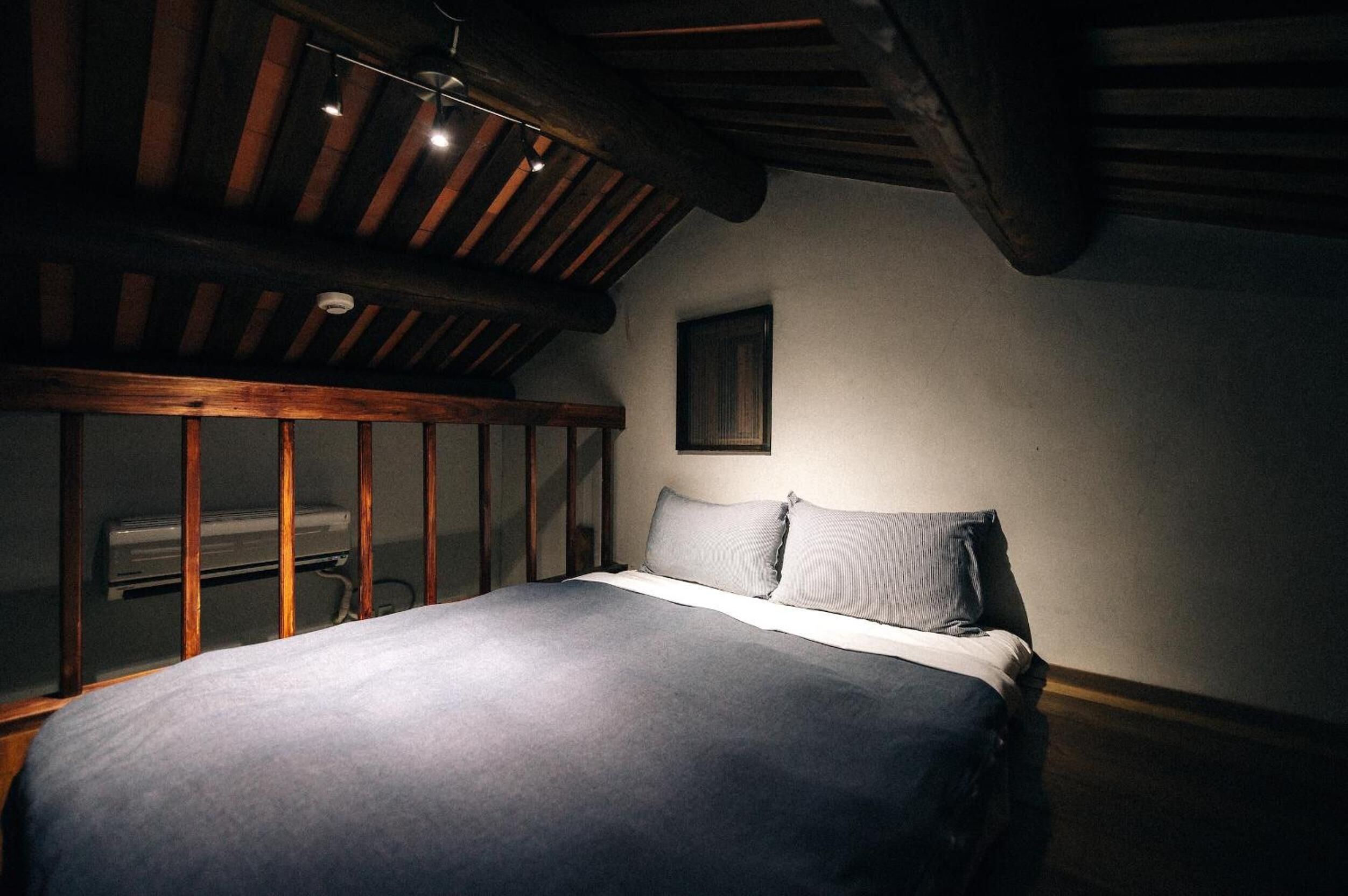 Een slaapkamer met een houten plafond, een bed met grijze beddengoed en een klein fotolijstje aan de muur.
