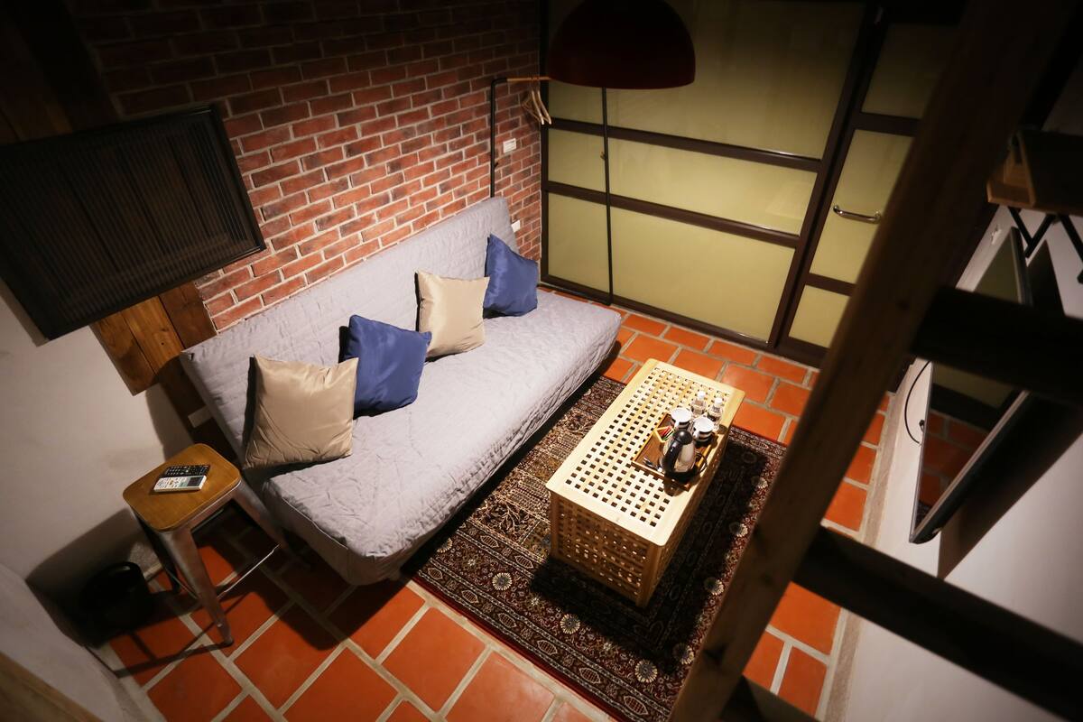 A cozy room with a grey sofa, a small wooden table with a tray, and a patterned rug on a tiled floor.