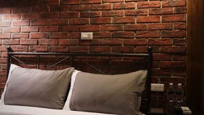 A bed with a metal frame and two pillows, a brick wall, a round ceiling light, and a small table with bottles and a remote control. - Kinba Guest House (Jinning)