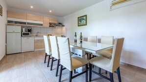 Una cocina moderna con armarios blancos, microondas y cafetera. Hay una mesa de comedor con sillas y un cuadro en la pared.