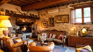 A cozy living room with a stone wall, wooden beams, a fireplace, and various decorative items. - Agriturismo Azienda Agricola il Pozzo (Capolona)