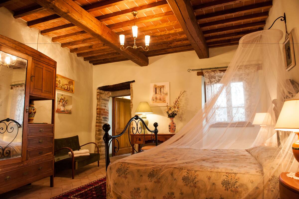 A bedroom with a wooden ceiling, a bed with a canopy, a nightstand, a dresser, and a chair.