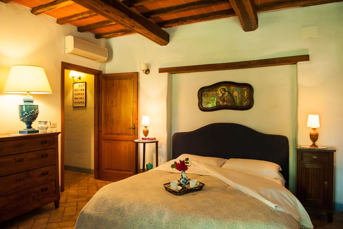 A bedroom with a bed, wooden dresser, bedside tables, and a wall-mounted painting.