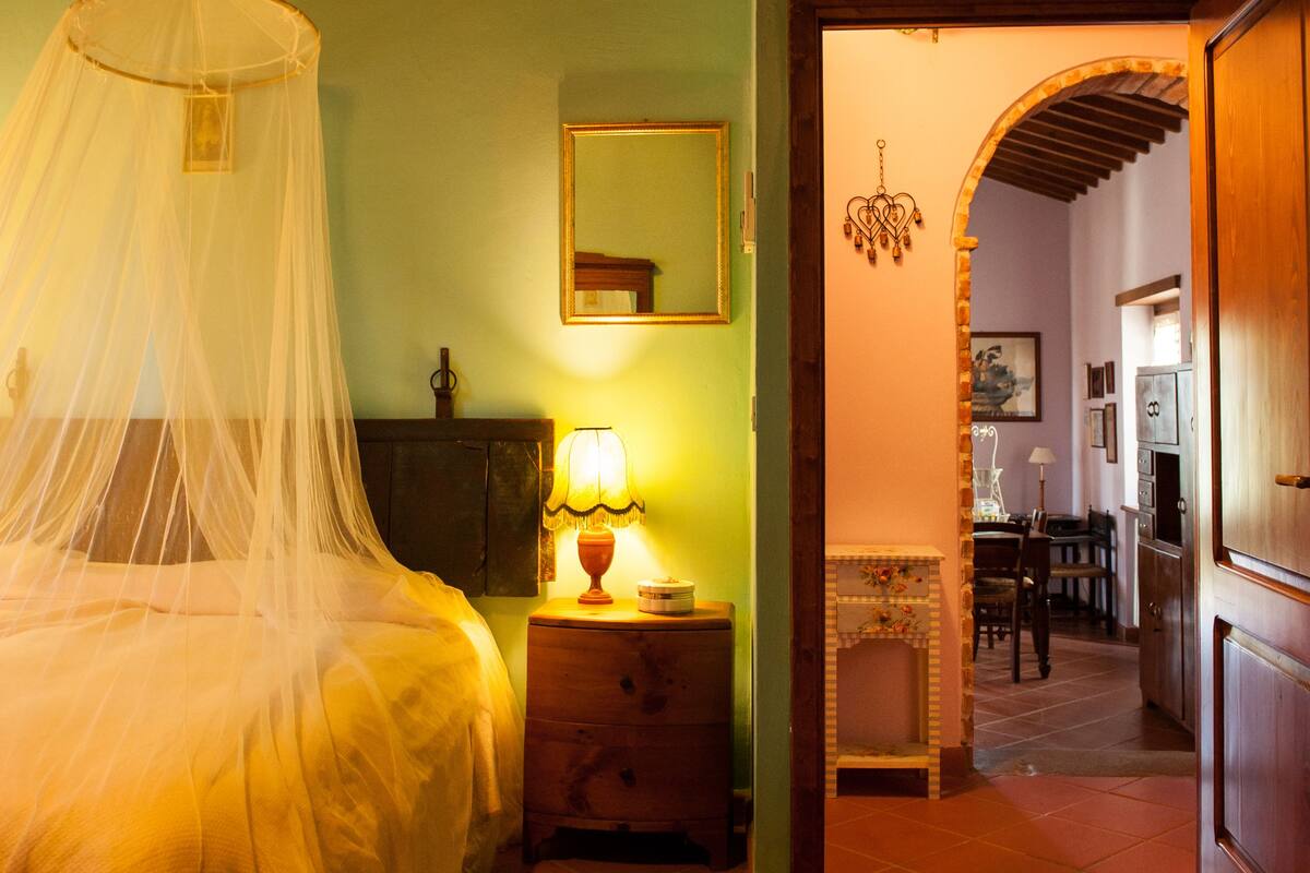 A bedroom with a bed, bedside lamp, air conditioning unit, and a hallway leading to a dining area.