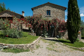 Una casa de piedra con jardín, un sendero de grava y un árbol alto.