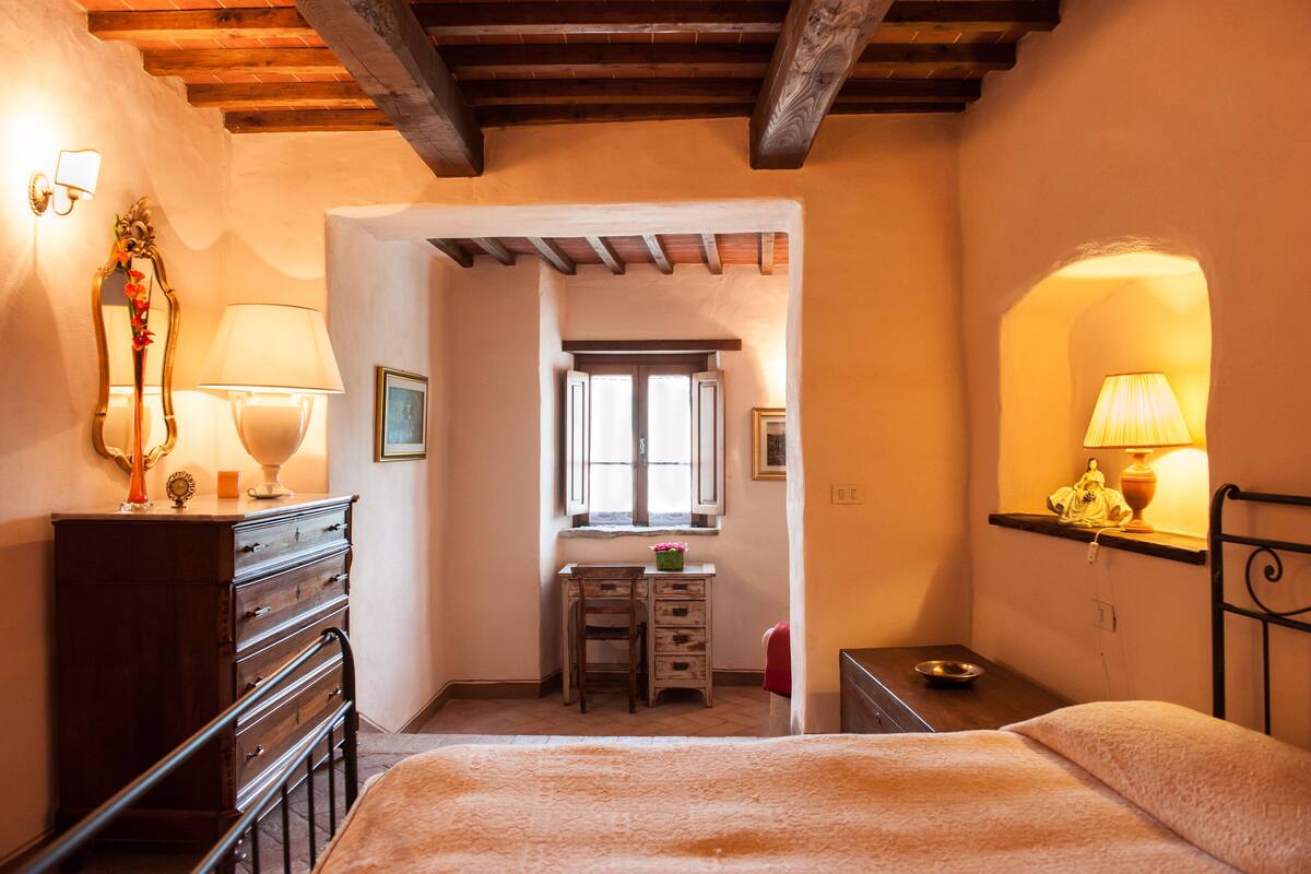 A bedroom with a wooden ceiling, a bed, a desk with a chair, and a window.