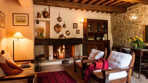 A cozy living room with a fireplace, wooden furniture, and stone walls. - Agriturismo Azienda Agricola il Pozzo (Capolona)