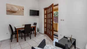 Uma sala de jantar com uma mesa, cadeiras, televisão na parede e uma porta de madeira que dá para o exterior.