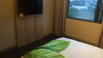 Een hotelkamer met een bed, een flatscreen televisie bevestigd aan een houten paneel, en een raam met gordijnen.