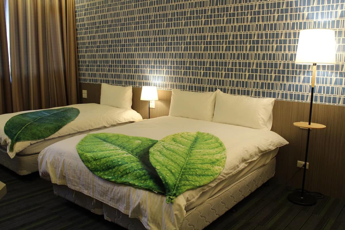 A hotel room with two beds, each with a green leaf-shaped pillow, a patterned wall, and a standing lamp.