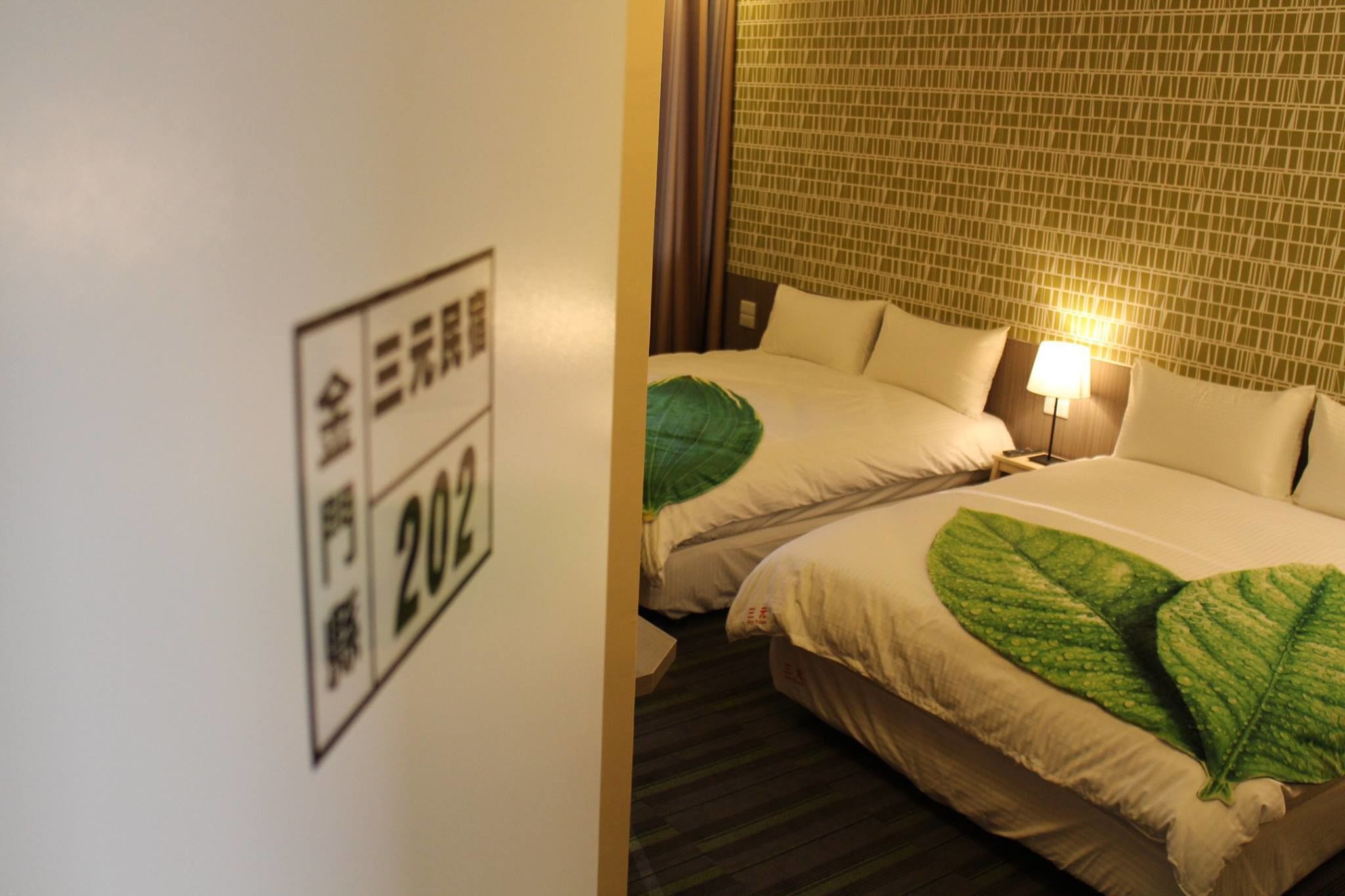 Quarto de hotel com duas camas, colcha com padrão de folhas verdes, parede com desenho em mosaico e um letreiro com caracteres japoneses.