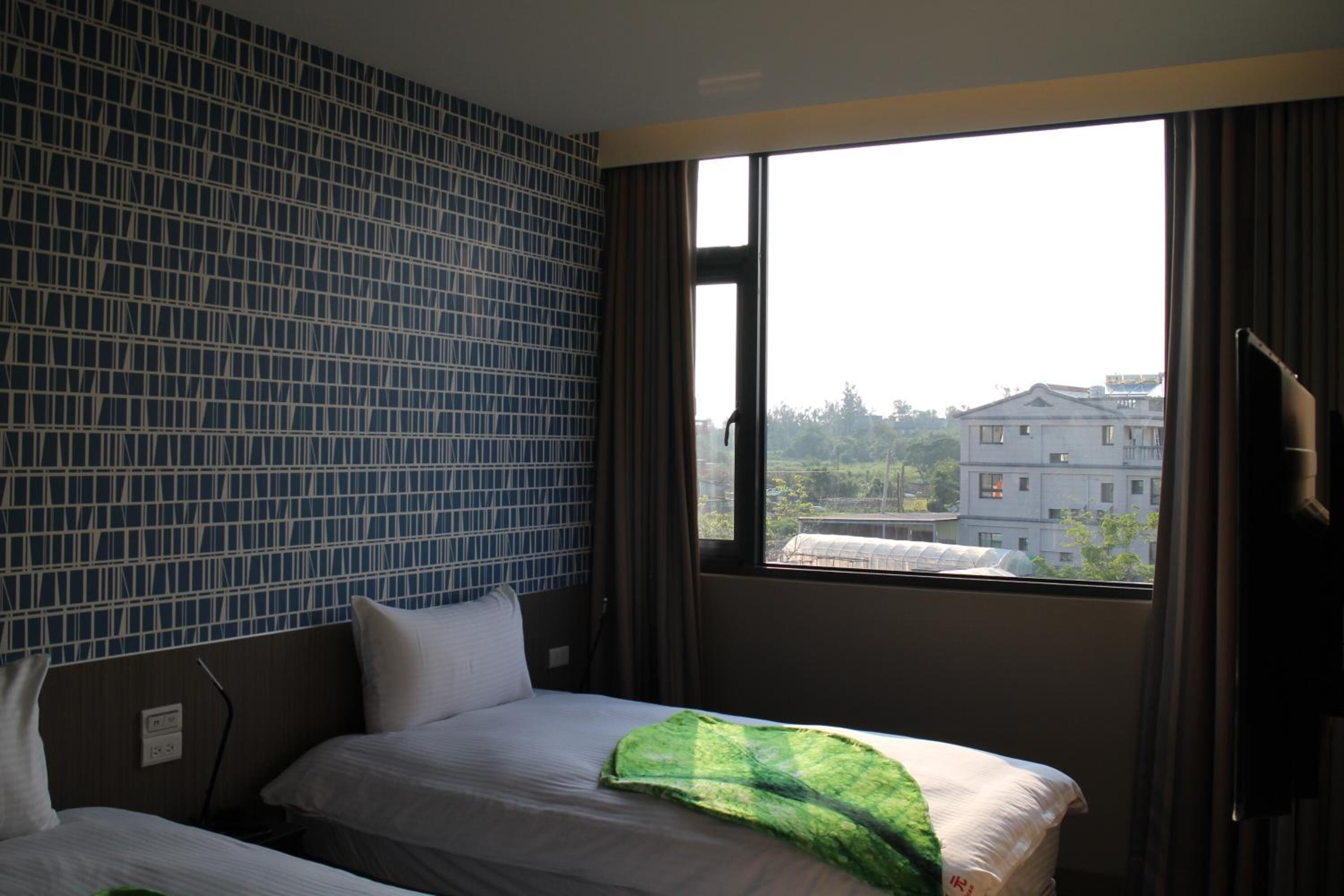 A hotel room with a large window, a bed with white linens, and a blue patterned wall.