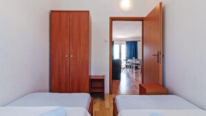 A room with two beds, a wooden wardrobe, and a door leading to a dining area. - 1 bedroom amazing apartment in Mandre (Mandre)