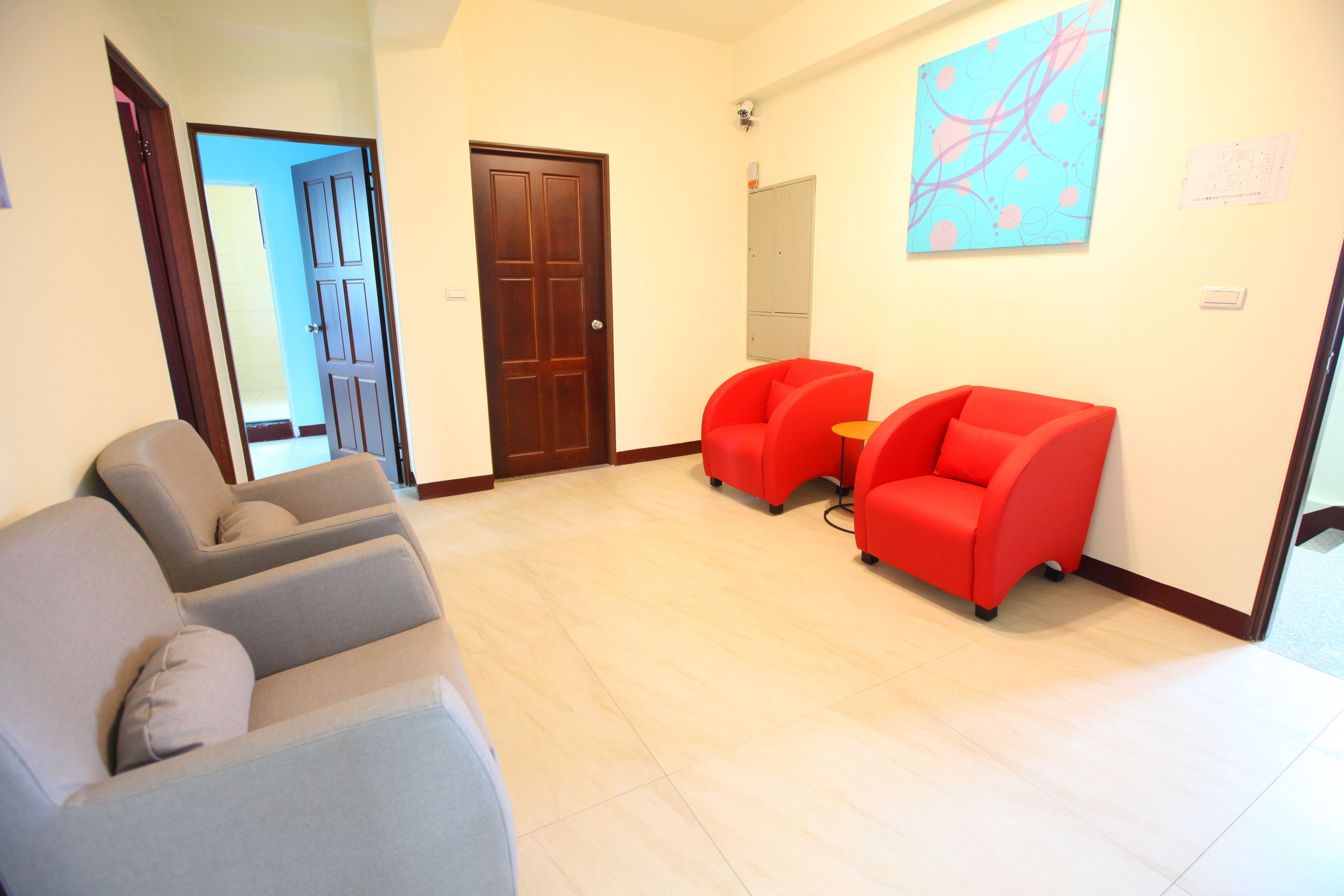 Una sala de estar con un sofá gris, un sillón rojo y una puerta de madera.