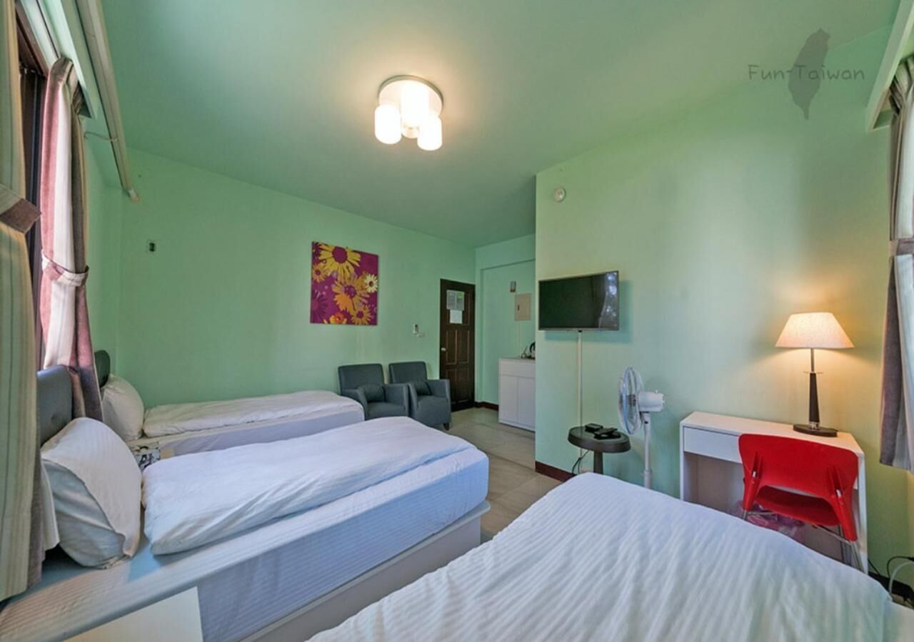 Habitación de hotel con dos camas individuales, un escritorio con lámpara, televisión y una silla roja.