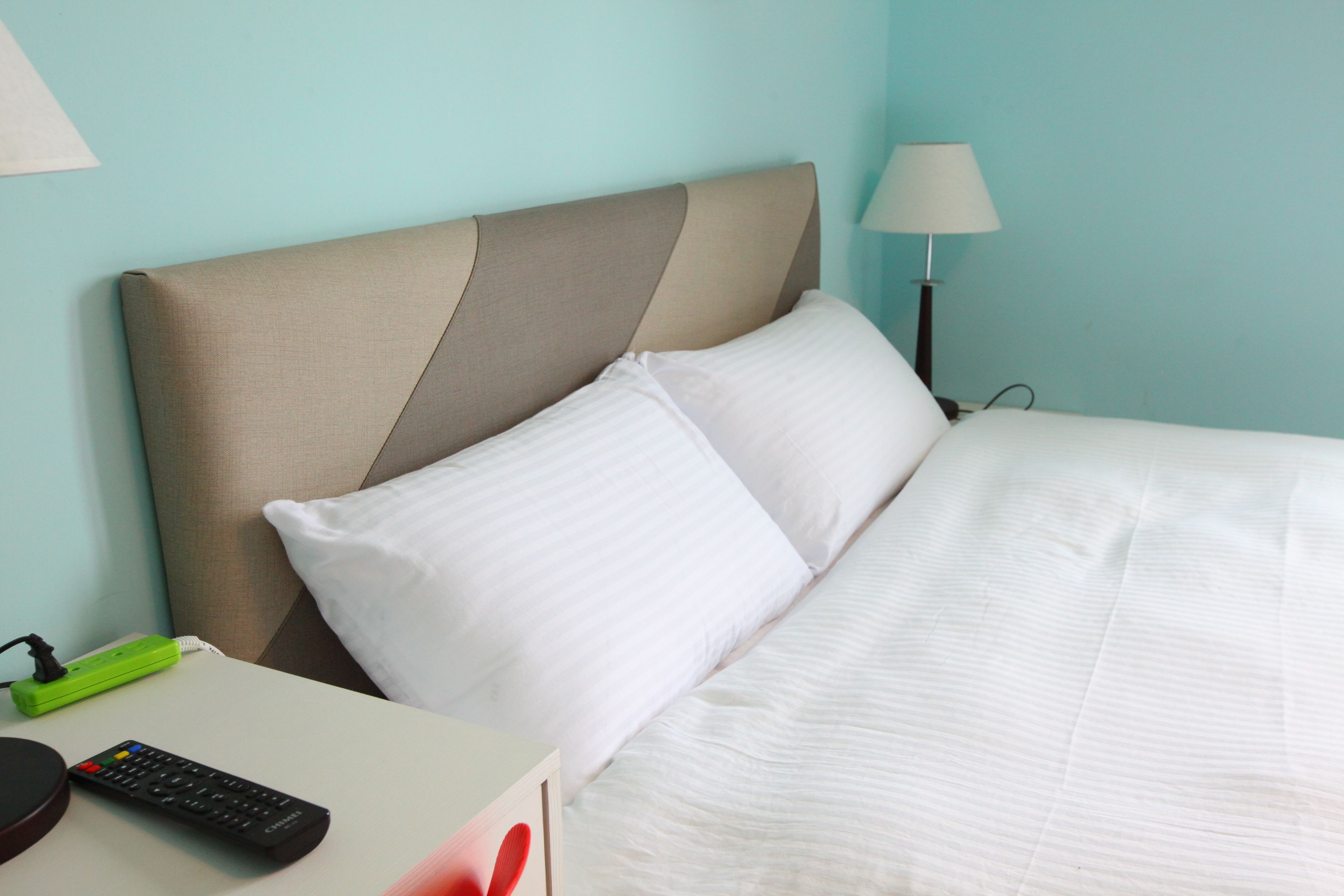 Una habitación de hotel con cama, almohadas blancas, mesita de noche y lámpara.