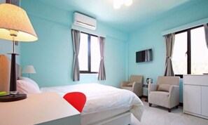 Una habitación de hotel con cama, escritorio, silla, aire acondicionado y televisor.